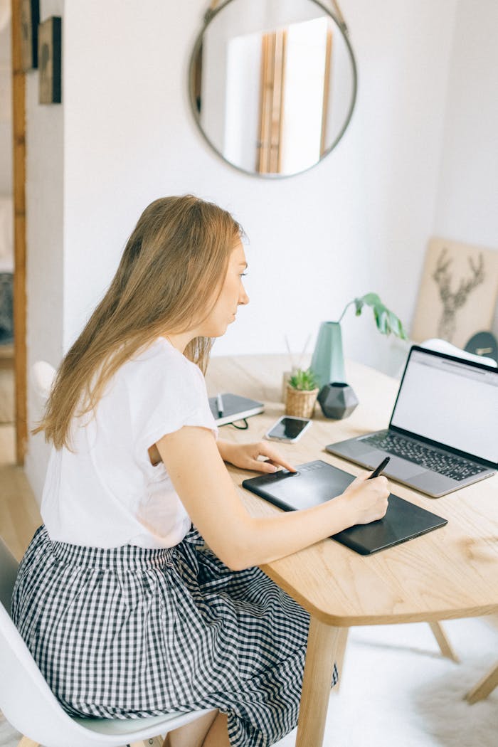 Woman in White Shirt Using Macbook Air on Brown Wooden Table